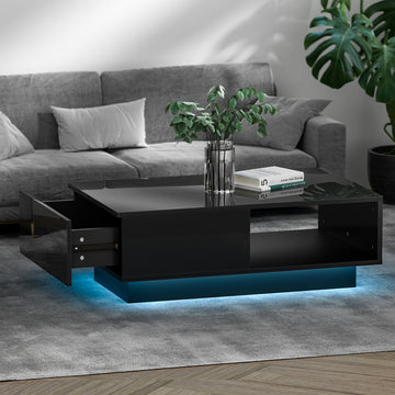 Black high-gloss LED coffee table in living room, drawer pulled open, blue LED base, plant vase and books on top, grey sofa