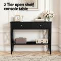 Black hall table in elegant entryway with 2 drawers, flowers on top and travel cases on lower shelf, 