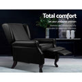 Black faux leather wingback recliner with footrest extended in dark scene, reclines 100 to 135 degrees, Total comfort text