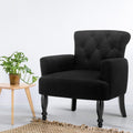 Black linen button-tufted armchair with turned wooden legs in white room with monstera plant on wood side table and jute rug