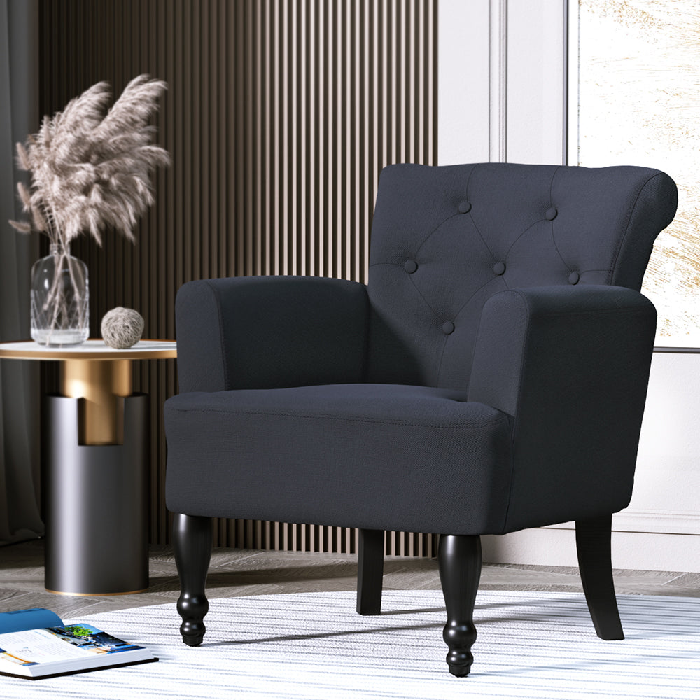 Black linen button-tufted armchair in dark styled room, gold side table with pampas grass vase and floor rug