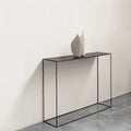 Slim black metal console table against cream wall with two white ceramic vases on top, grey concrete floor