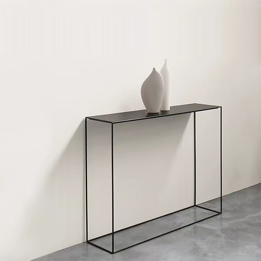 Slim black metal console table against cream wall with two white ceramic vases on top, grey concrete floor
