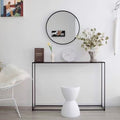 Slim black metal console table in entryway with round mirror above, styled with clock, vases and eucalyptus branches