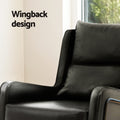 Close-up of black PU leather armchair back and wing in room with window, 