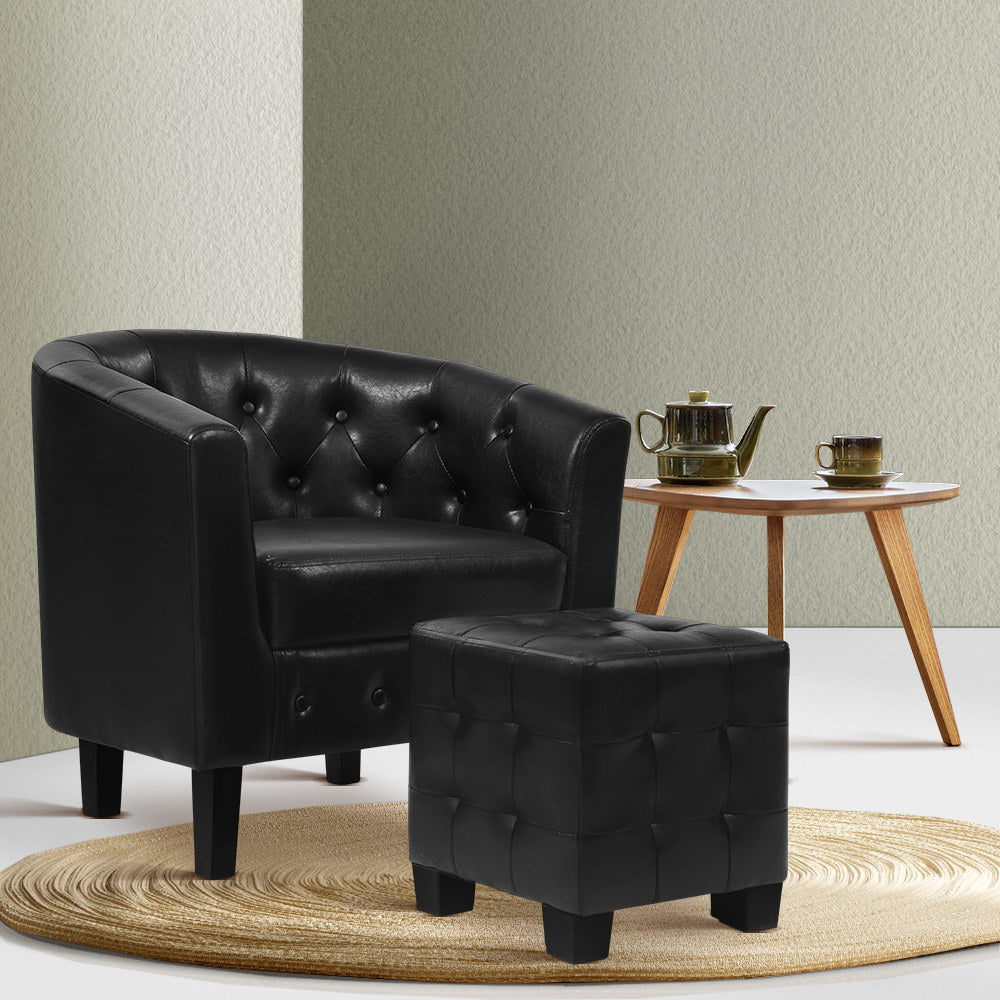 Black PU leather tub chair and ottoman on round rattan rug beside wooden side table with teapot, sage green wall, front angle