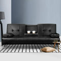 Black PU leather sofa bed with cupholder tray holding two white cups on striped rug, teapot on side table