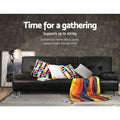 Black PU leather sofa bed with polka dot cushions and rainbow throw against dark concrete wall, gathering text