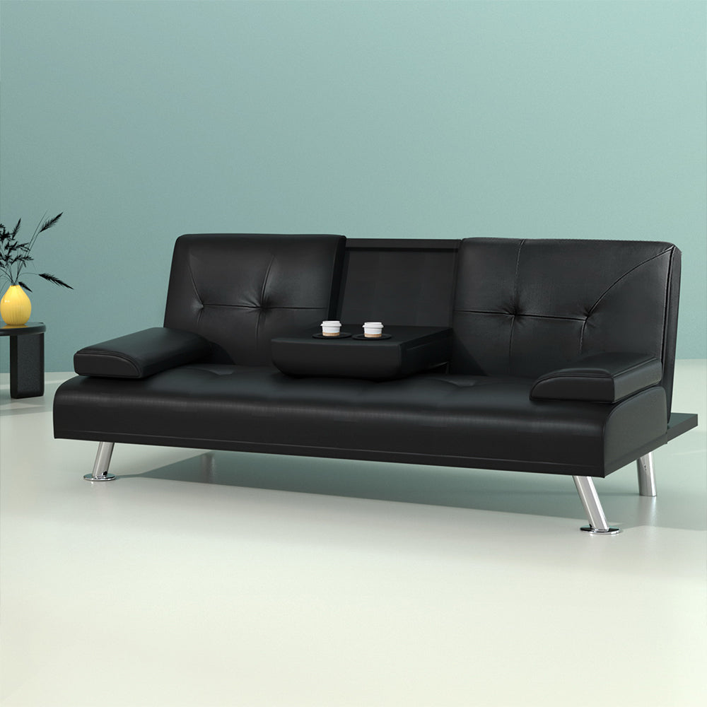 Black PU leather sofa bed with open cupholder and two cups against teal wall, yellow vase on black side table