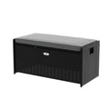 Black rattan outdoor storage bench with grey cushion on top, silver badge on front, three-quarter angle, white background