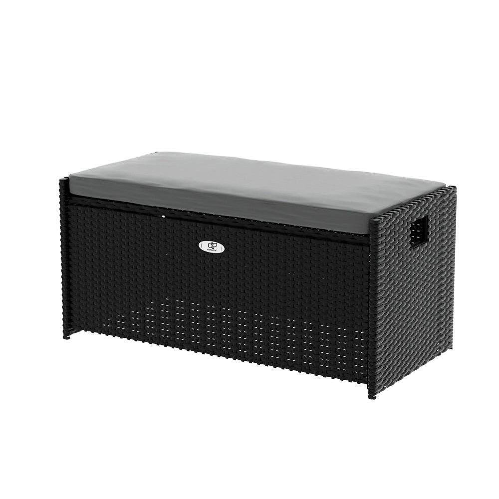 Black rattan outdoor storage bench with grey cushion on top, silver badge on front, three-quarter angle, white background