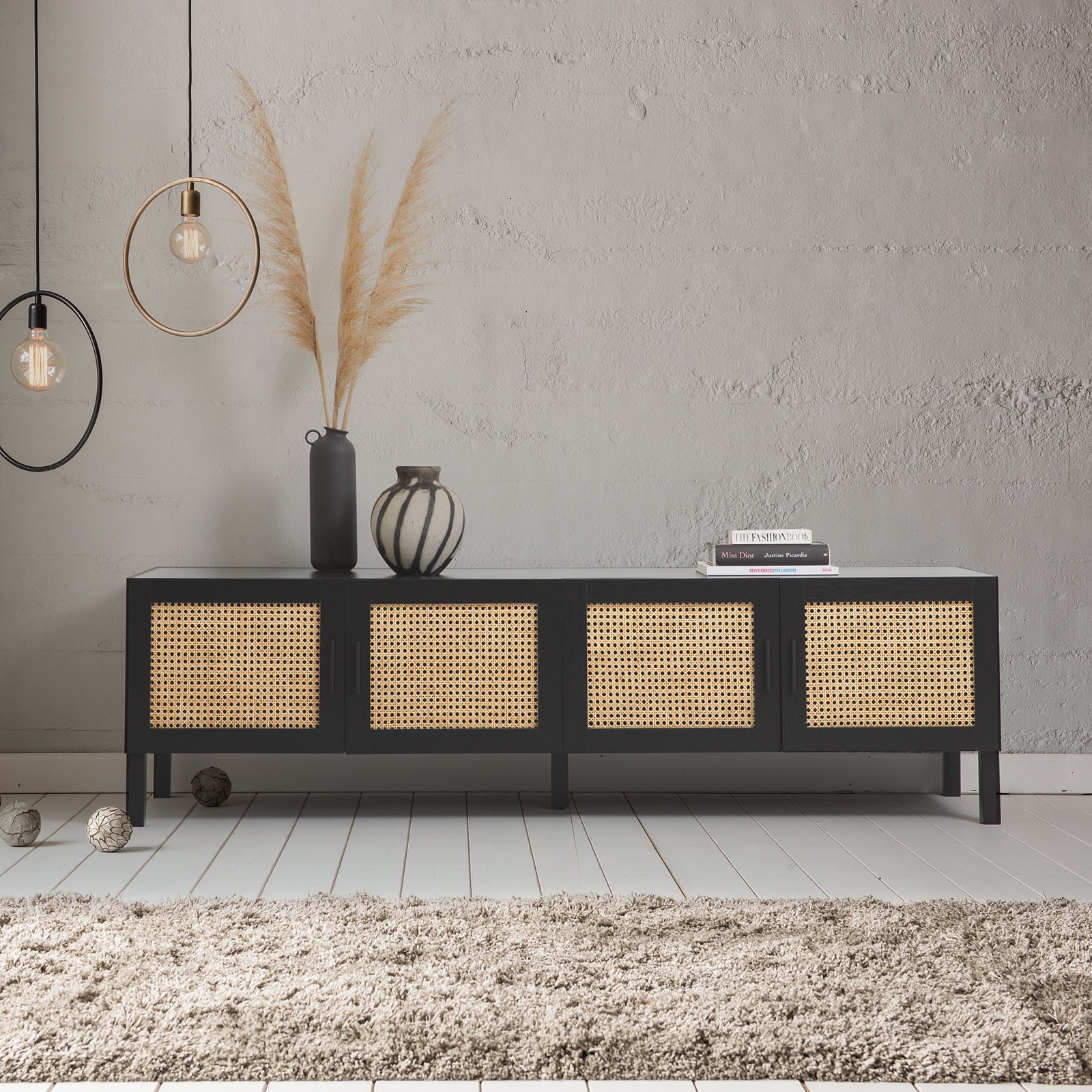 Black rattan TV unit lifestyle in grey concrete room with pampas grass vase dark vessels books and pendant lights
