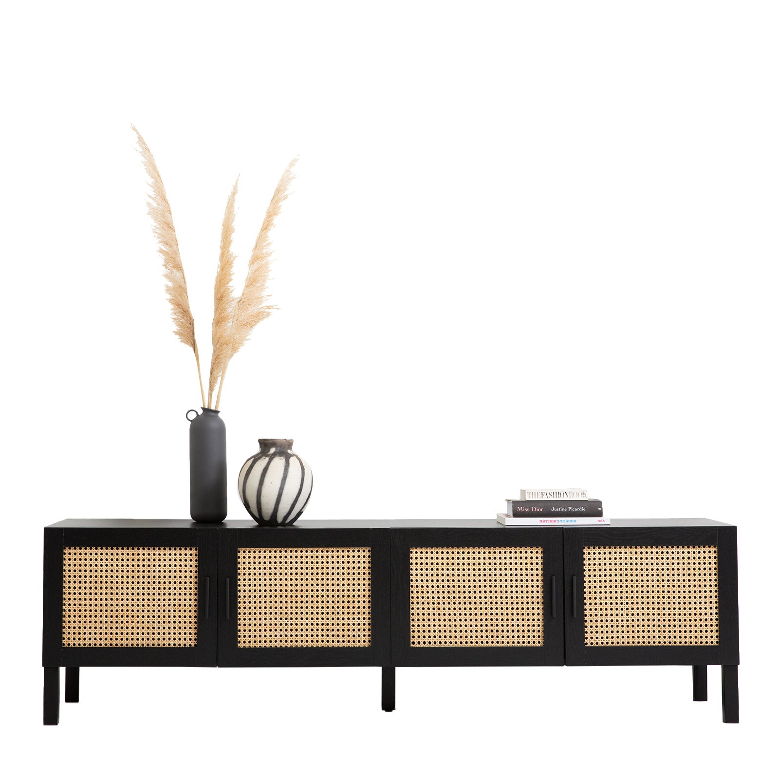 Black rattan TV unit on white with pampas grass dark vase striped vase and stacked fashion books on top