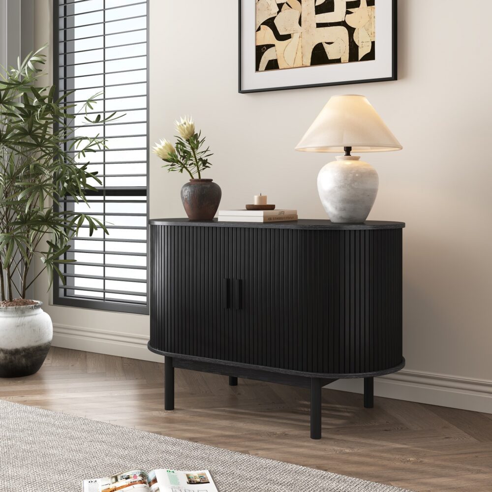 Black reeded sideboard angled view in room with shuttered window, abstract wall art, table lamp and flower vase on top