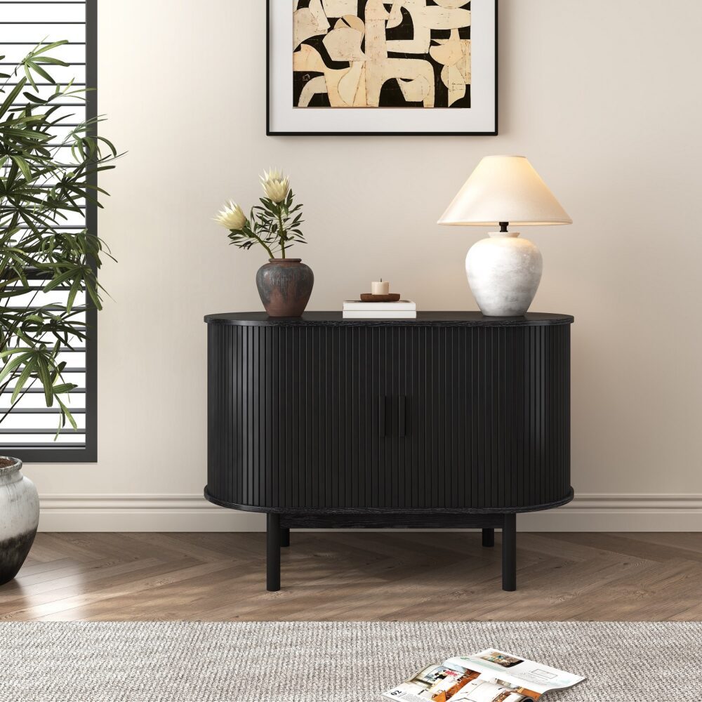 Black reeded sideboard with rounded ends in room setting, two ceramic vases and books on top, shuttered window behind