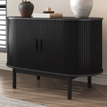 Black reeded sideboard with rounded ends in room setting, two ceramic vases and books on top, shuttered window behind