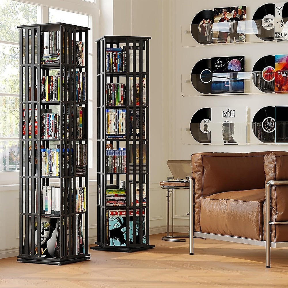 Two black rotating tower bookshelves filled with DVDs and books in music room with vinyl records on wall and leather armchair
