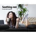 Woman in pyjamas lying on black suede floor lounger flat holding a mug with palm plant in background