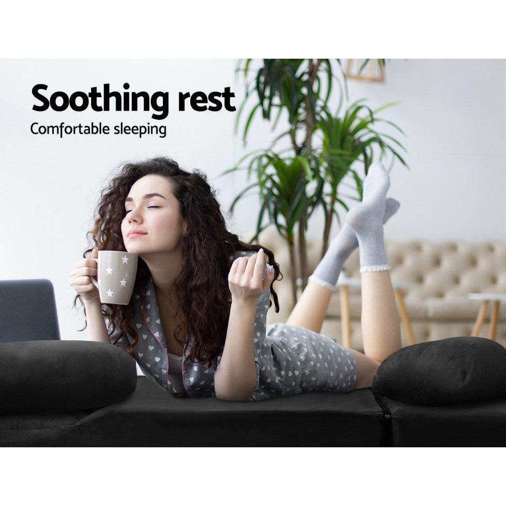 Woman in pyjamas lying on black suede floor lounger flat holding a mug with palm plant in background