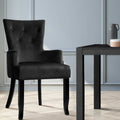 Black velvet wingback armchair beside dark side table on herringbone floor against light blue panelled wall