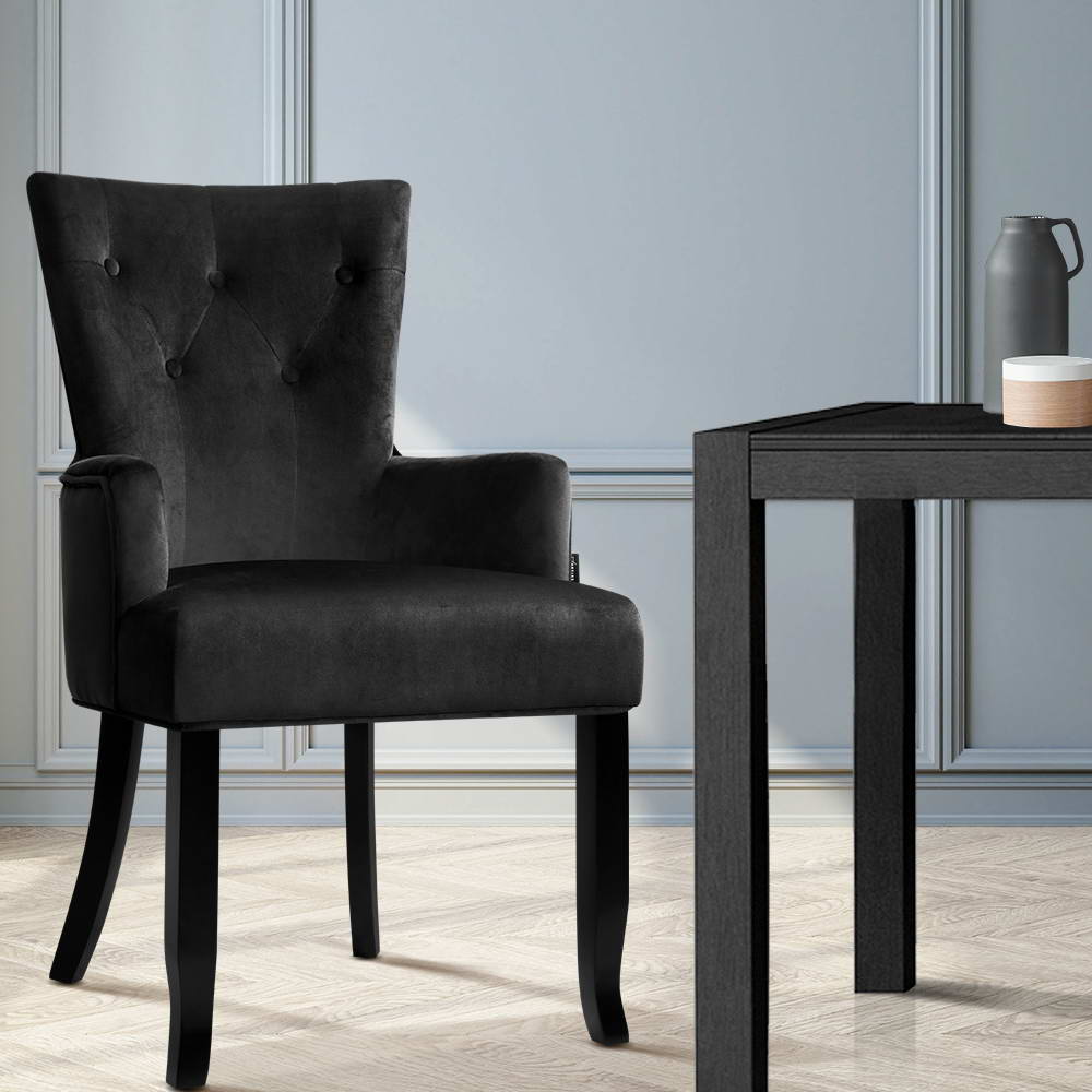 Black velvet wingback armchair beside dark side table on herringbone floor against light blue panelled wall