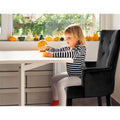 Black velvet button-tufted armchair with child seated at white desk beside window with pumpkins on sill in lifestyle room