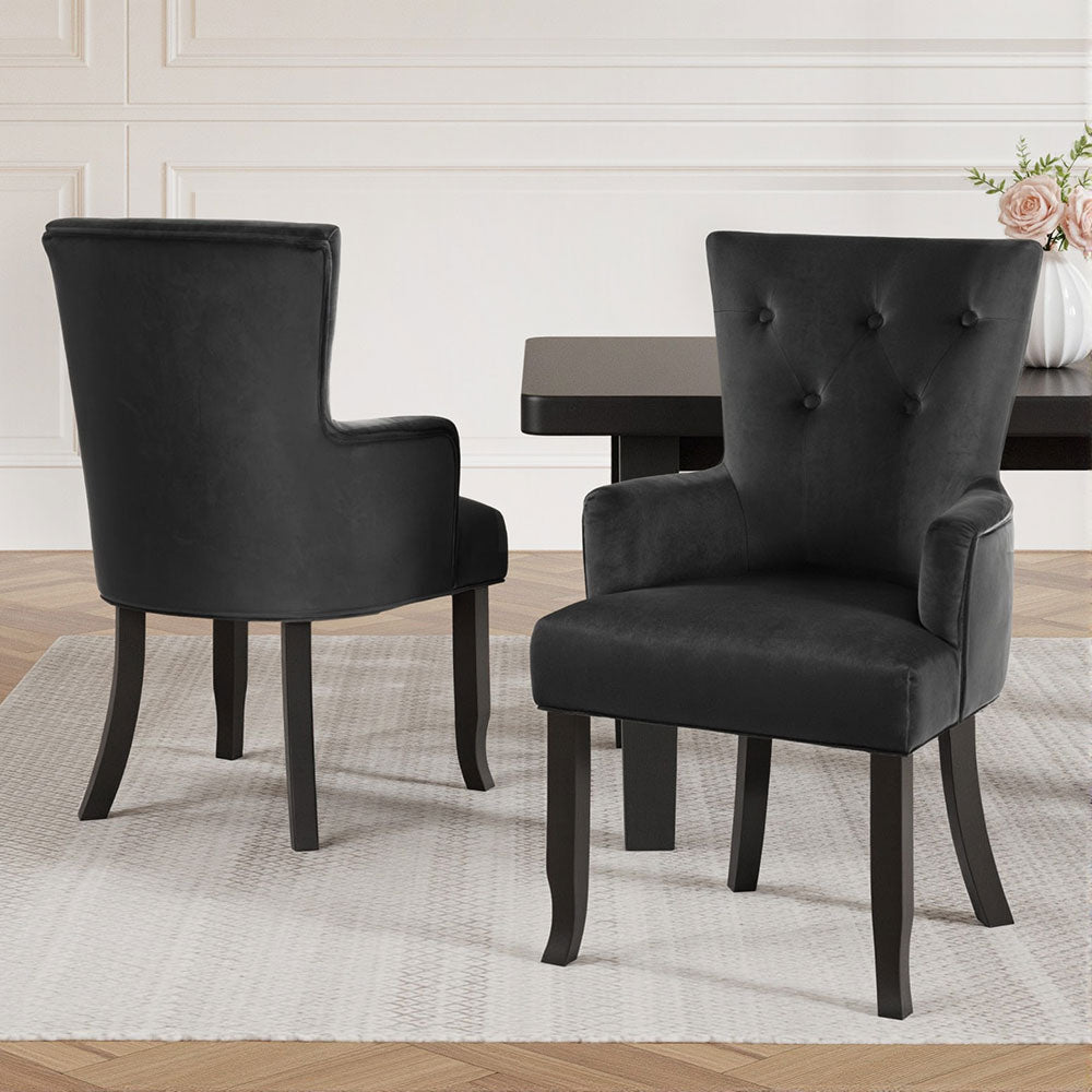 Two black velvet wingback dining chairs in room: front tufted backrest and rear view, roses and dark table visible