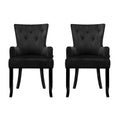 Pair of black velvet button-tufted wingback dining chairs, front view on white background, diamond button pattern visible