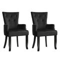 Pair of black velvet button-tufted wingback dining chairs with curved black legs, three-quarter angle on white background