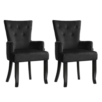 Pair of black velvet button-tufted wingback dining chairs with curved black legs, three-quarter angle on white background