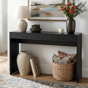 Black wood-grain console table in hallway with lamp, dark vases, orange flowers on top and wicker basket on lower shelf