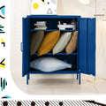 Navy blue metal locker open in room showing pillows stacked on lower shelves, books and decorative items on top shelf