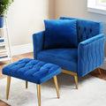 Blue velvet armchair with cushion and tufted ottoman in room setting with bookshelf, cream rug, window and gold legs