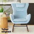Light blue velvet rocking chair in room with wood side table and plant, 