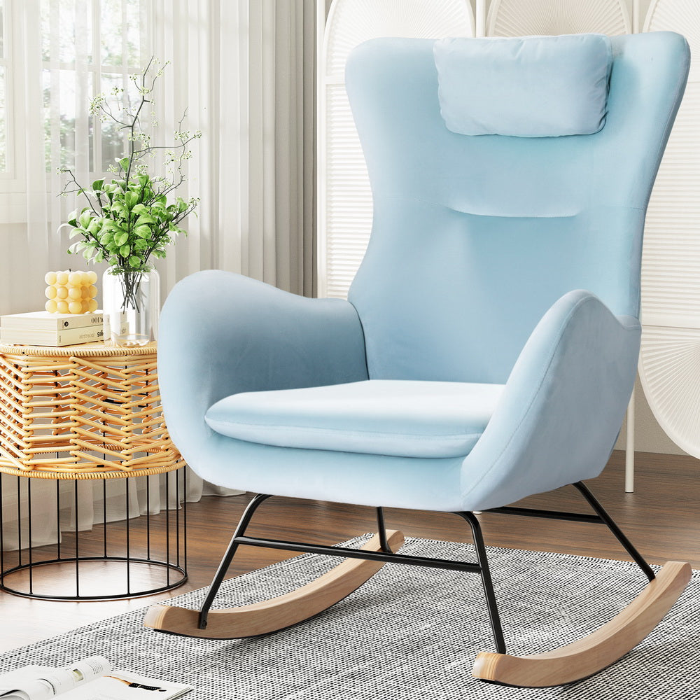 Light blue velvet wingback rocking chair with headrest pillow and wood runners, lifestyle shot with wicker table and plant