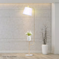 Arc floor lamp with side table lit against concrete wall, white flower vase on side table, bare branch vase beside it