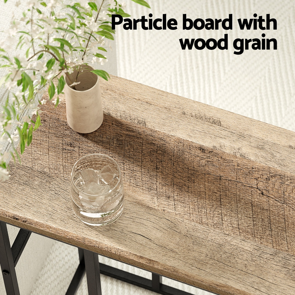 Close-up of a wood grain particle board table top with a glass and small vase styled on the surface.