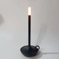 Matte black candle-style LED table lamp with ring handle on round base, warm white glow at top, white background