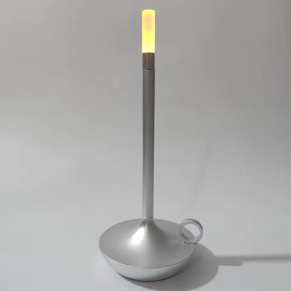 Silver candle-style LED table lamp with ring handle on round base, warm amber glow at top, grey background