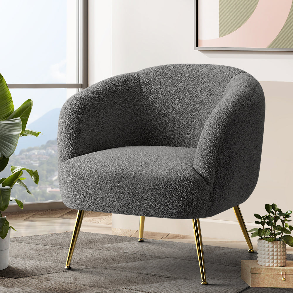 Charcoal grey boucle tub chair with rounded barrel back and gold metal tapered legs in living room near window