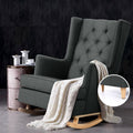 Charcoal tufted wingback rocking chair with white throw beside vintage pink nightstand, dark stone wall background