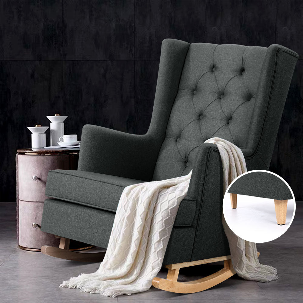 Charcoal tufted wingback rocking chair with white throw beside vintage pink nightstand, dark stone wall background