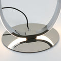 Close-up of polished chrome round base with warm LED light reflecting off surface, lamp loop joint above