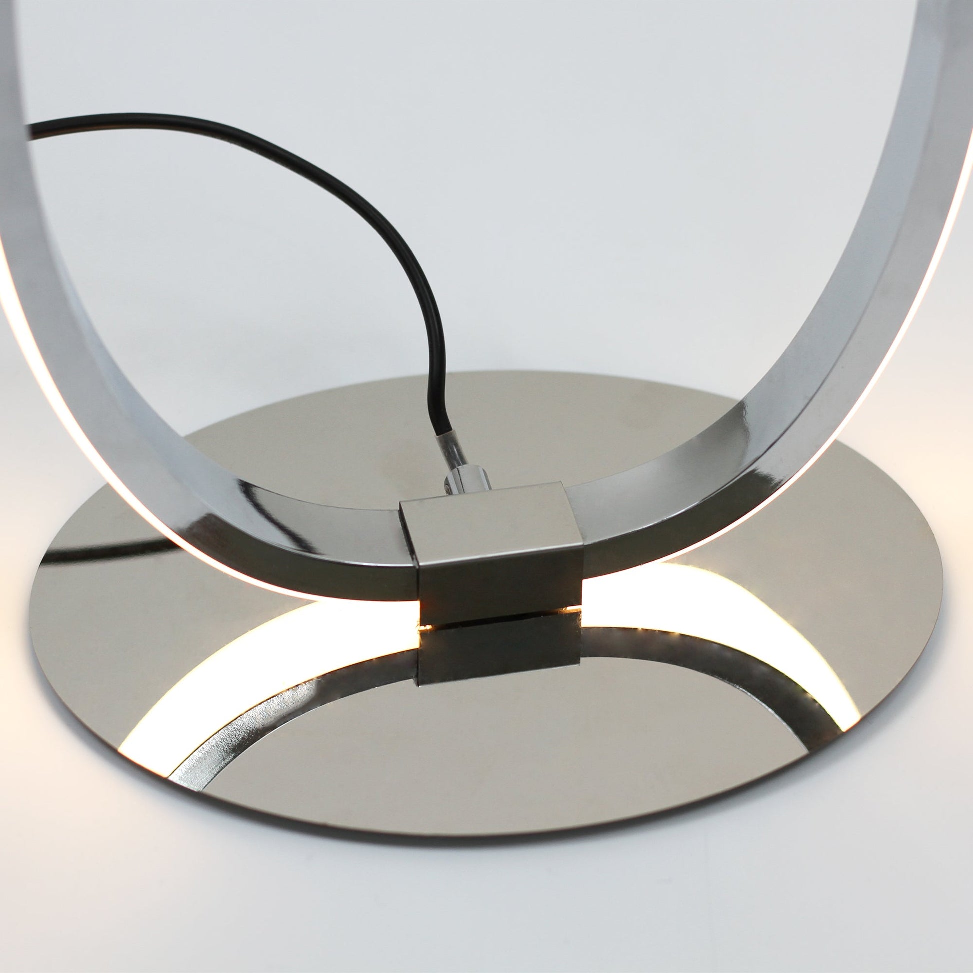 Close-up of polished chrome round base with warm LED light reflecting off surface, lamp loop joint above