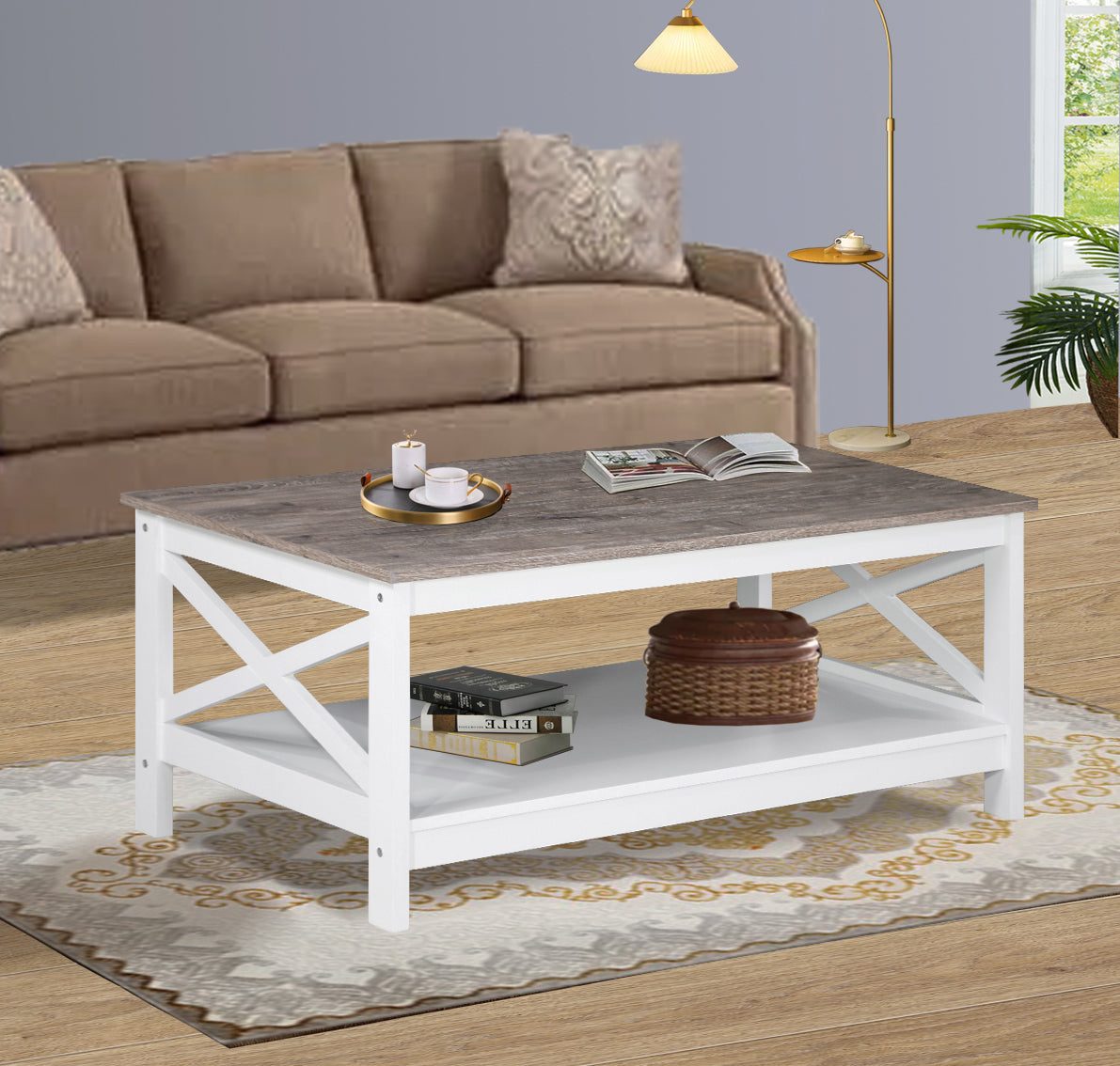 Coffee table with grey top and white X-frame in room setting with tan sofa, candles on top and books with basket on shelf