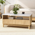 Coffee table with marble top styled with plant and coffee cup, books on open shelf, fluted drawers, beige sofa behind
