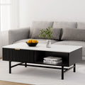 White marble-top coffee table with black ribbed sliding drawer and open shelf, styled with oranges in a bowl and a plant