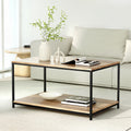 Rectangular two-tier coffee table with wood-grain top and black metal frame in a living room with a beige sofa, vase, and