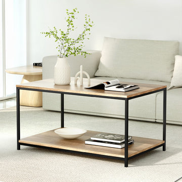 Rectangular two-tier coffee table with wood-grain top and black metal frame in a living room with a beige sofa, vase, and