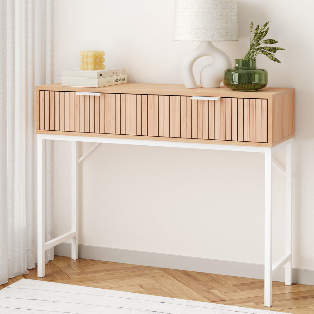Console table with fluted oak drawer front, white X-frame metal legs, styled with books and green glass vase in room